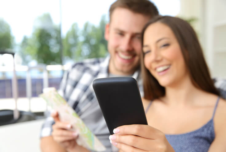 Happy couple of tourists consulting smart phone content in an hotel room